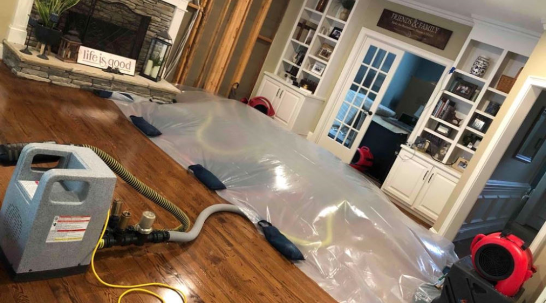 A living room featuring a large, plastic-covered area with drying equipment and fans, indicating water damage restoration efforts.